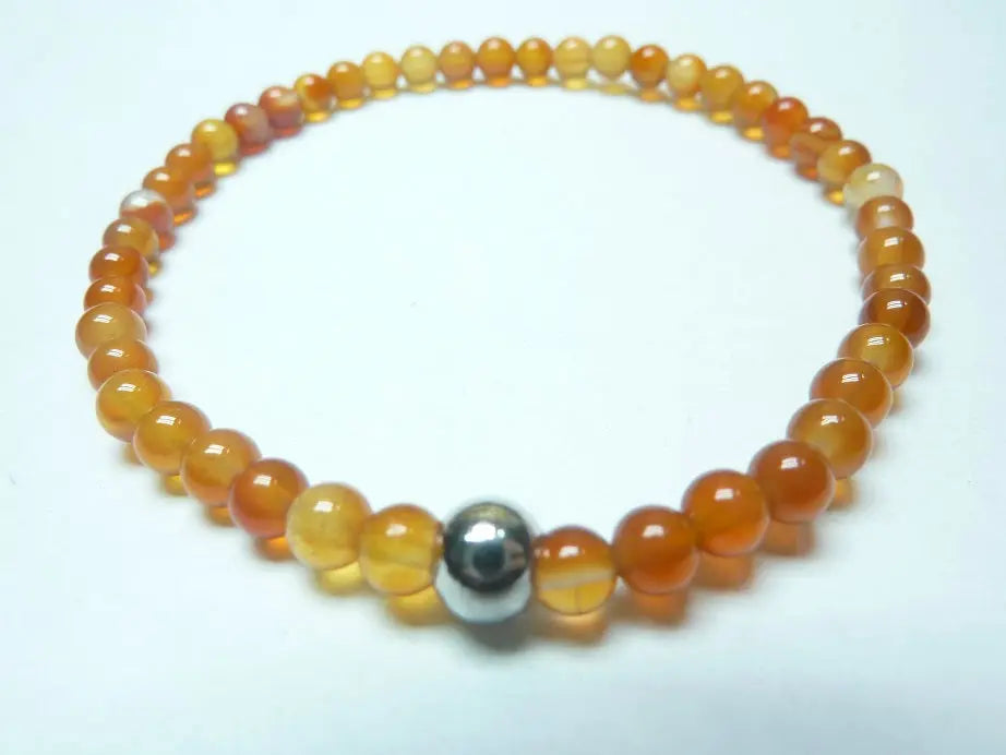 Bracelet en cornaline naturelle avec perles rondes orange vif et une perle métallique centrale, monté sur fil élastique robuste.