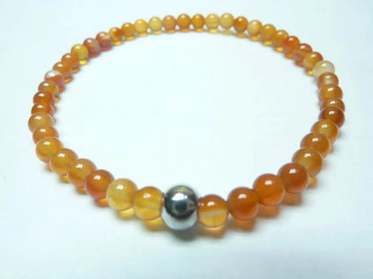 Bracelet en cornaline naturelle avec perles rondes orange vif et une perle métallique centrale, monté sur fil élastique robuste.